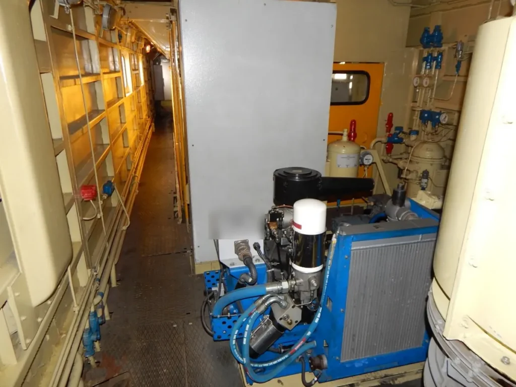 Oil-flooded air compressor unit with blue frame, oil filter and air-oil cooler in an equipment room